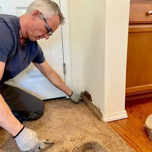 Chris trimming and securing a carpet edge at the baseboard during the same threshold repair