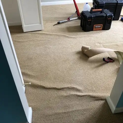 A ripple standing up in the carpet at a doorway, tools set down beside it