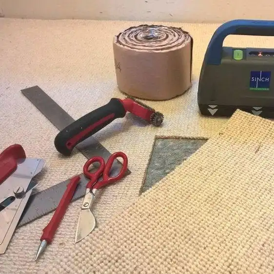 Seaming tools, seam tape and a triangular carpet patch laid flat on beige carpet